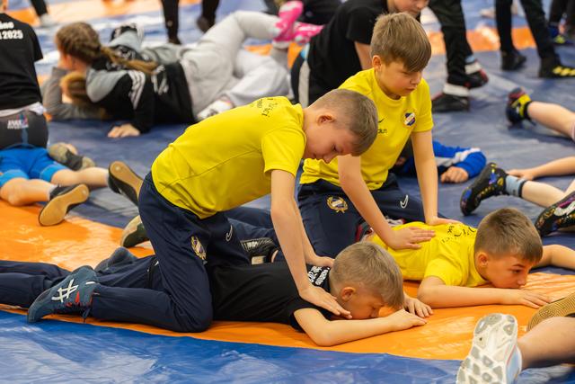 Boys in yellow jerseys practice wrestling holds on an orange mat, focused and engaged during a youth sports session.