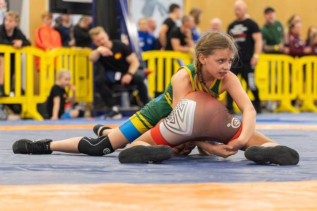 Determined girl in green singlet pins her opponent to the blue mat, maintaining control with focused intensity.