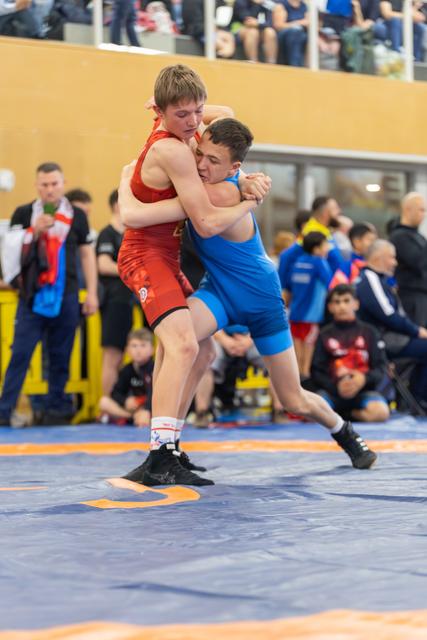 Two teenage wrestlers locked in a tight clinch, straining against each other with intense focus on a blue competition mat.