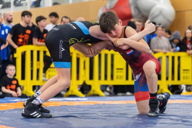 Two young wrestlers locked in a tight clinch, both leaning forward intensely during a youth match on a blue mat.