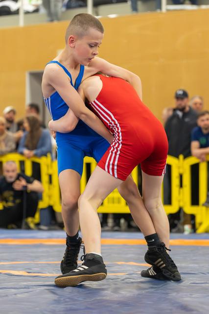 Two young wrestlers lock in a fierce clinch on the mat, both focused and determined during a competitive bout.