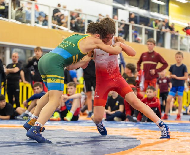 Two young wrestlers lock arms in fierce concentration, one in green-yellow, one in red, competing before a crowd.