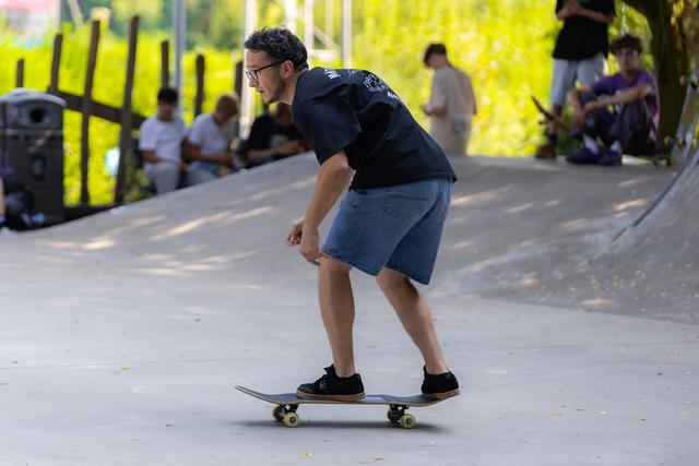Man skateboarding through a park pathway, crouched in concentration with spectators watching in the background
