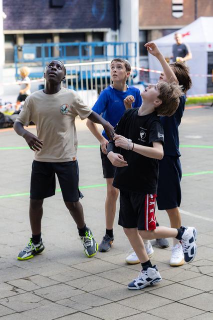 Three boys look up tracking a ball during an outdoor game, showing focus and anticipation on a paved court