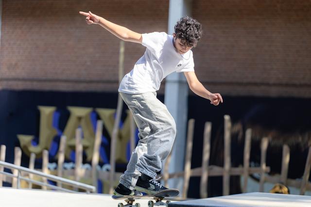 Young skateboarder with curly hair performing a balancing trick on ramp, arms extended for stability in outdoor skatepark