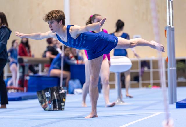Young athlete performs arabesque balance with arms extended during floor exercise at indoor sports venue