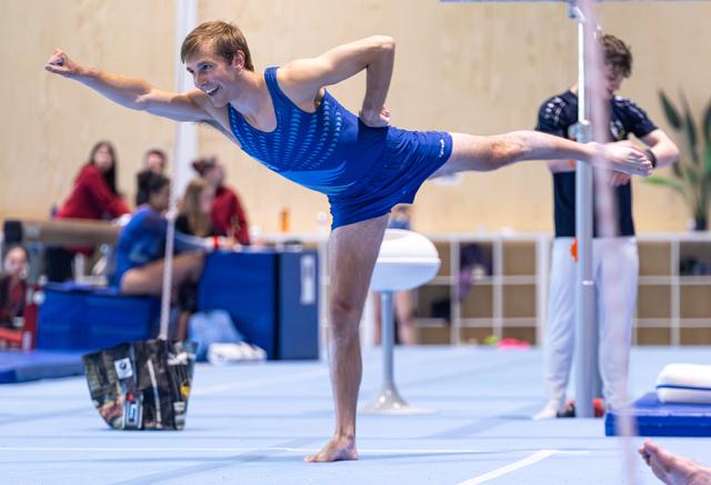 Young athlete balances gracefully on prosthetic leg during floor routine, beaming with joy and confidence at indoor event