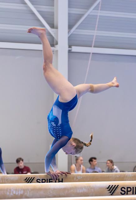 Young gymnast performs an inverted handstand on the balance beam, legs split vertically, during a training session
