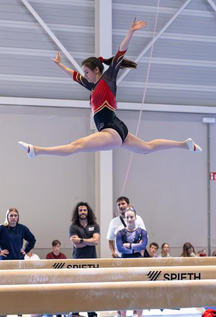 Female gymnast performs impressive split leap with extended arms above balance beam during training session
