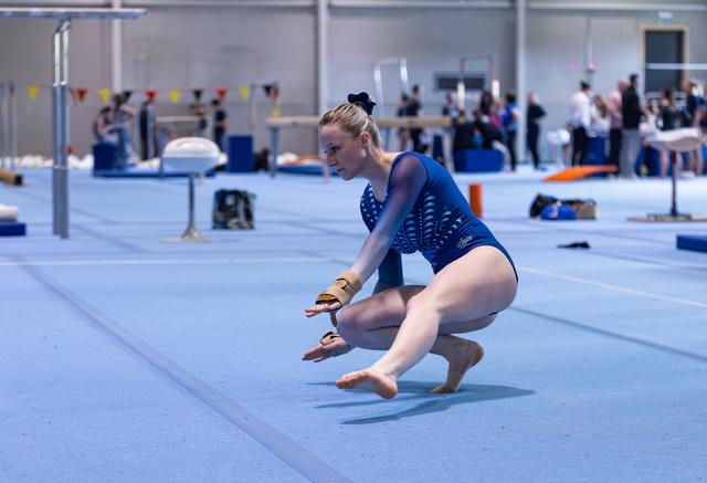 Young athlete executing a floor routine landing on blue mat, arms extended mid-performance in training facility