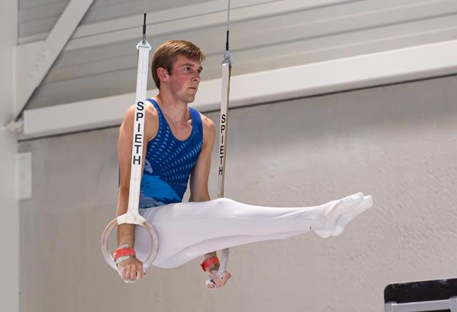 Young male athlete performing a horizontal hold on the rings, displaying intense concentration and strength