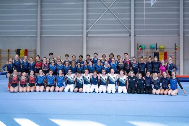 Large group of athletes in matching uniforms pose together on blue training floor in gymnasium
