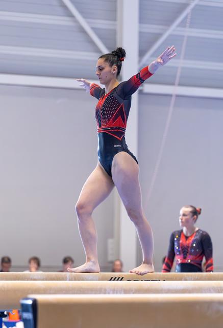 Gymnast performs on balance beam with arms extended, displaying concentration and poise during her routine