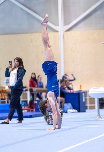 Young athlete performs vertical handstand on floor mat during routine, demonstrating balance and strength in blue outfit