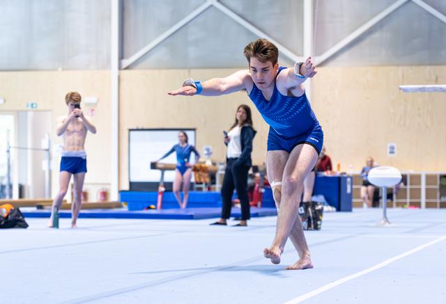 Young male performer executes floor routine with extended arms and focused expression in indoor sports facility