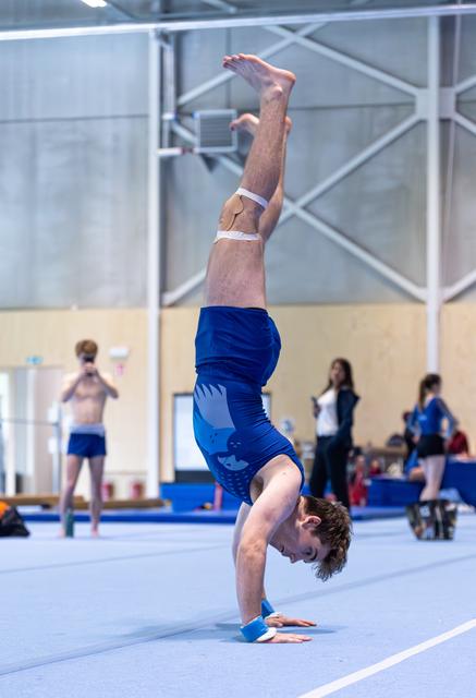 Male athlete performing a controlled handstand on the floor mat with straight legs extended upward during training