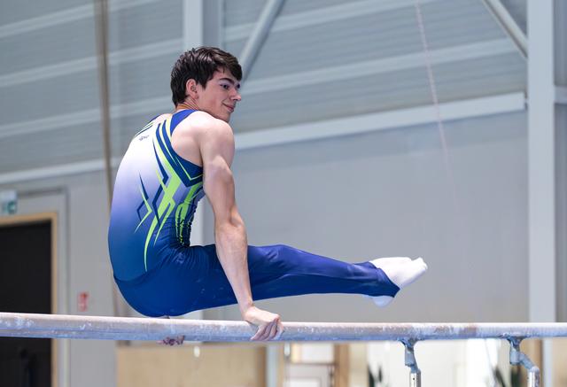 Young male athlete performing an L-sit hold on horizontal bar, looking back with a confident smile during routine