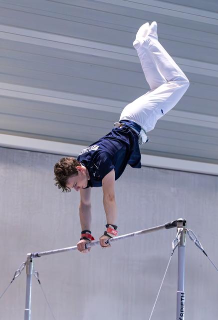 Young male gymnast performing an inverted handstand position on the high bar during a routine, legs extended upward