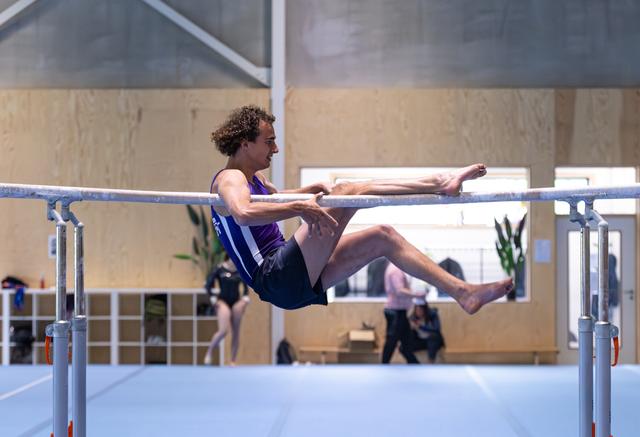 Male athlete performing a back lever hold on parallel bars, demonstrating strength and body control in a training facility
