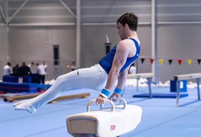 Male gymnast performs horizontal support position on pommel horse during training, demonstrating strength and control