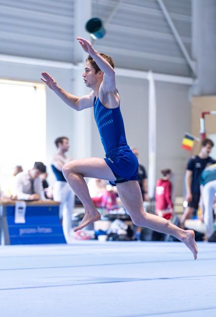 Male gymnast performs a split leap on floor exercise with arms extended overhead during training session