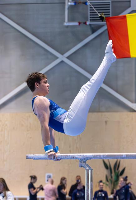 Male gymnast performs impressive V-sit hold on parallel bars during routine, demonstrating exceptional core strength and control