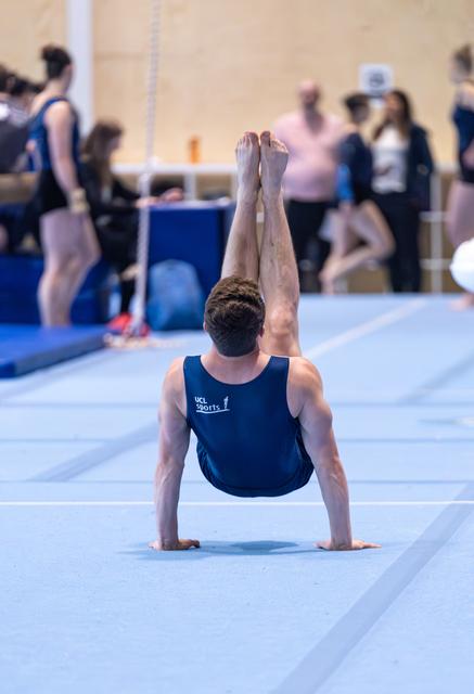 Male gymnast performs handstand balance on floor exercise mat during training session