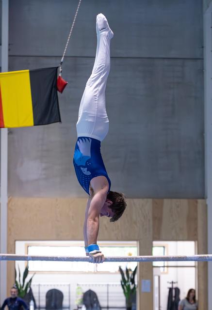Male gymnast performing precise handstand on high bar, body fully extended vertically during routine