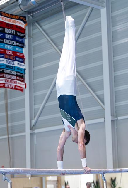 Male gymnast performing a handstand on the horizontal bar with straight legs pointed upward during a routine