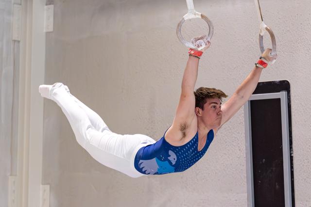 Young male gymnast performing an iron cross hold on still rings, displaying strength and concentration in a training facility