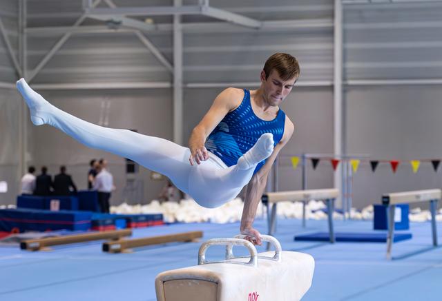 Male gymnast executing a horizontal leg hold on pommel horse, demonstrating strength and balance in training facility