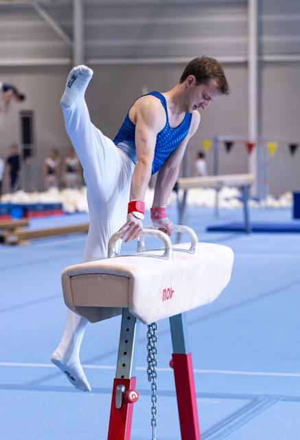 Young athlete performs pommel horse routine with legs extended, demonstrating strength and focus in training facility