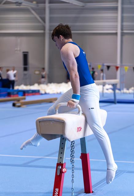 Male gymnast in blue and white uniform practicing on pommel horse in indoor training facility