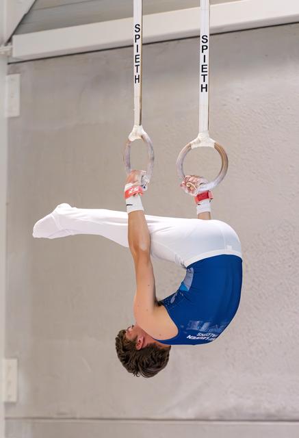 Young male athlete performs an inverted hang on still rings, displaying strength and control during training.