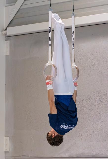 Young athlete hanging upside down on still rings, demonstrating strength and body control during training
