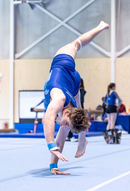 Young athlete in blue leotard executes a graceful backbend during floor routine, displaying flexibility and control