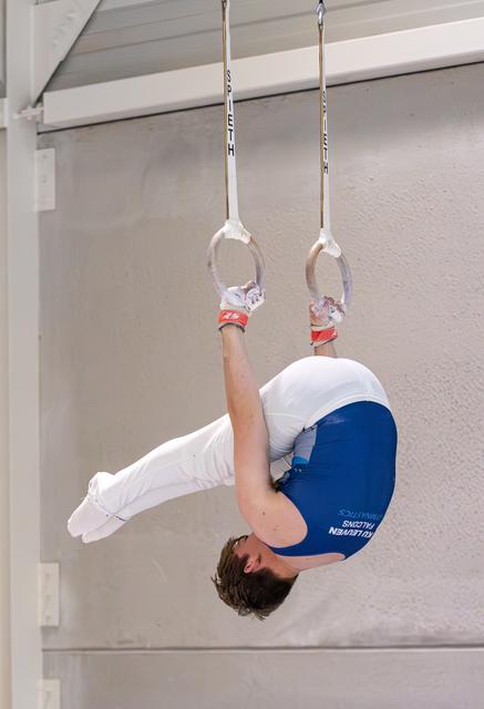 Young gymnast executing an inverted pike position on rings, demonstrating strength and control during training
