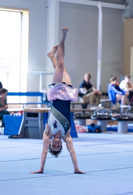 Young athlete performing a handstand during floor routine, legs split vertically in training facility