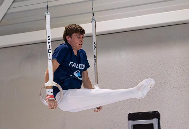 Boy in Falcon jersey holds horizontal position on still rings, demonstrating strength and focus during routine