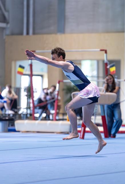 Young gymnast performs a dynamic floor routine leap, wearing a navy leotard and pink tutu in an indoor training facility