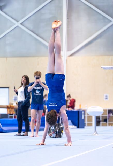 Young gymnast in blue leotard performs a vertical handstand on floor exercise mat during indoor training session