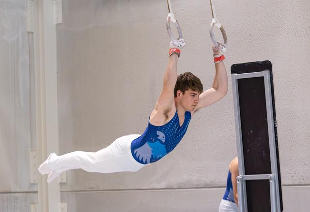 Young male athlete performing horizontal hold on rings with extended body position in white training hall