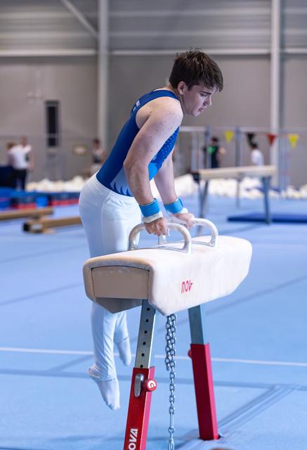 Male gymnast executes a move on the pommel horse, displaying concentration and strength in a training facility